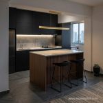 Modern linear gold LED hanging light with remote illuminating a luxury wood and black kitchen island in a Singapore BTO apartment.