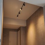 Black adjustable magnetic track light highlighting a condo hallway wall